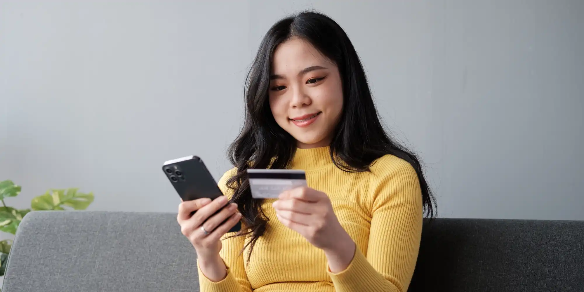 an asian woman, spurred to make a purchase while interacting with social media pulls out her credit card to pay on her phone